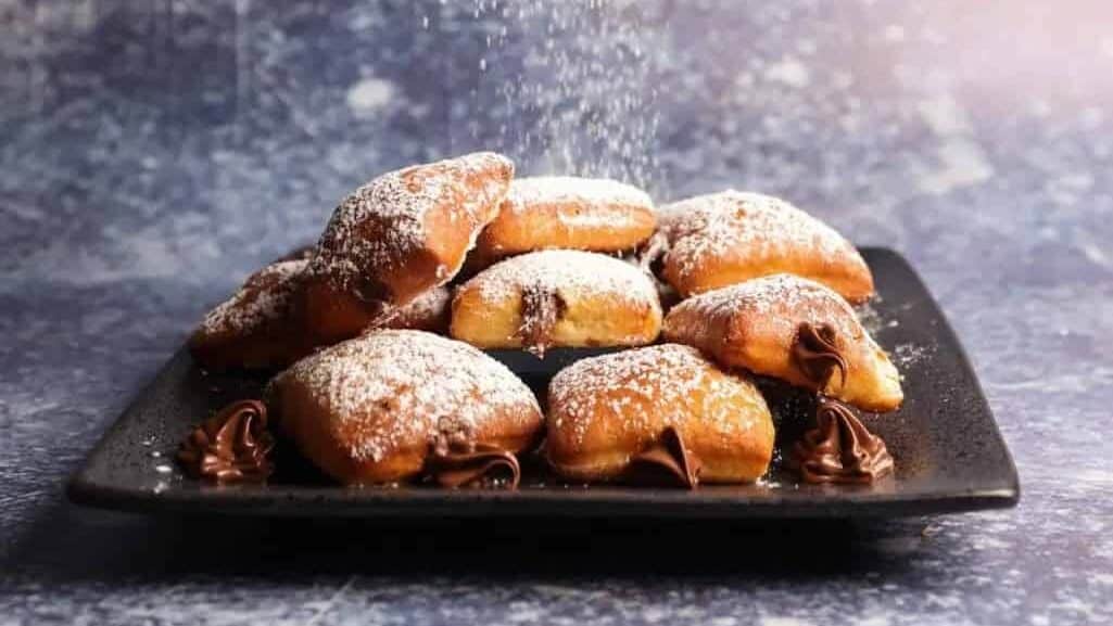 A hand is sprinkling powdered sugar on a plate of pastries.