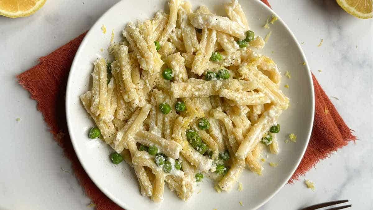 Penne pasta with lemon and peas on a white plate.