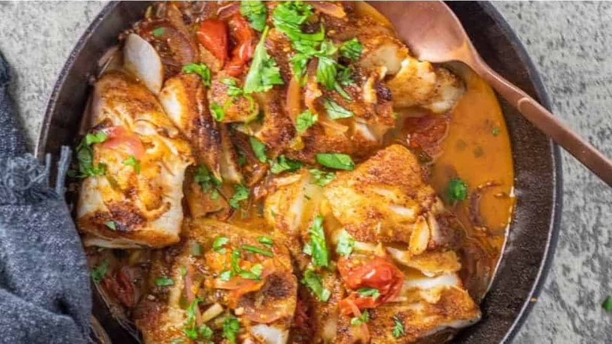 Fish in a skillet with tomatoes and parsley.