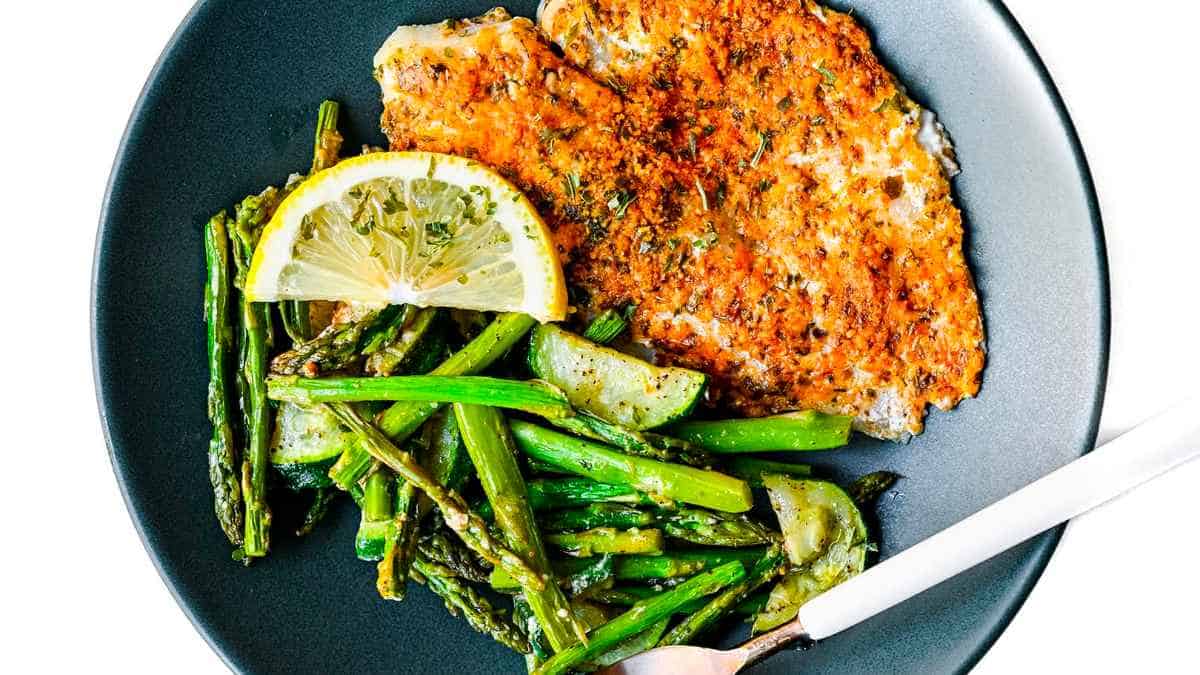 Fried fish with asparagus and lemon on a plate.
