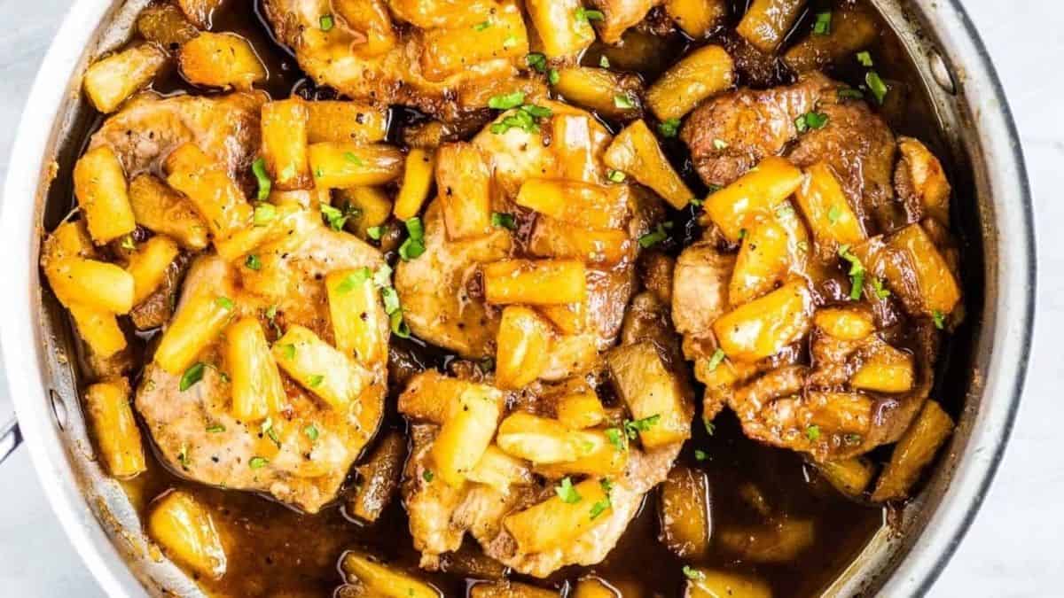 Pork chops in a skillet with apples and gravy.