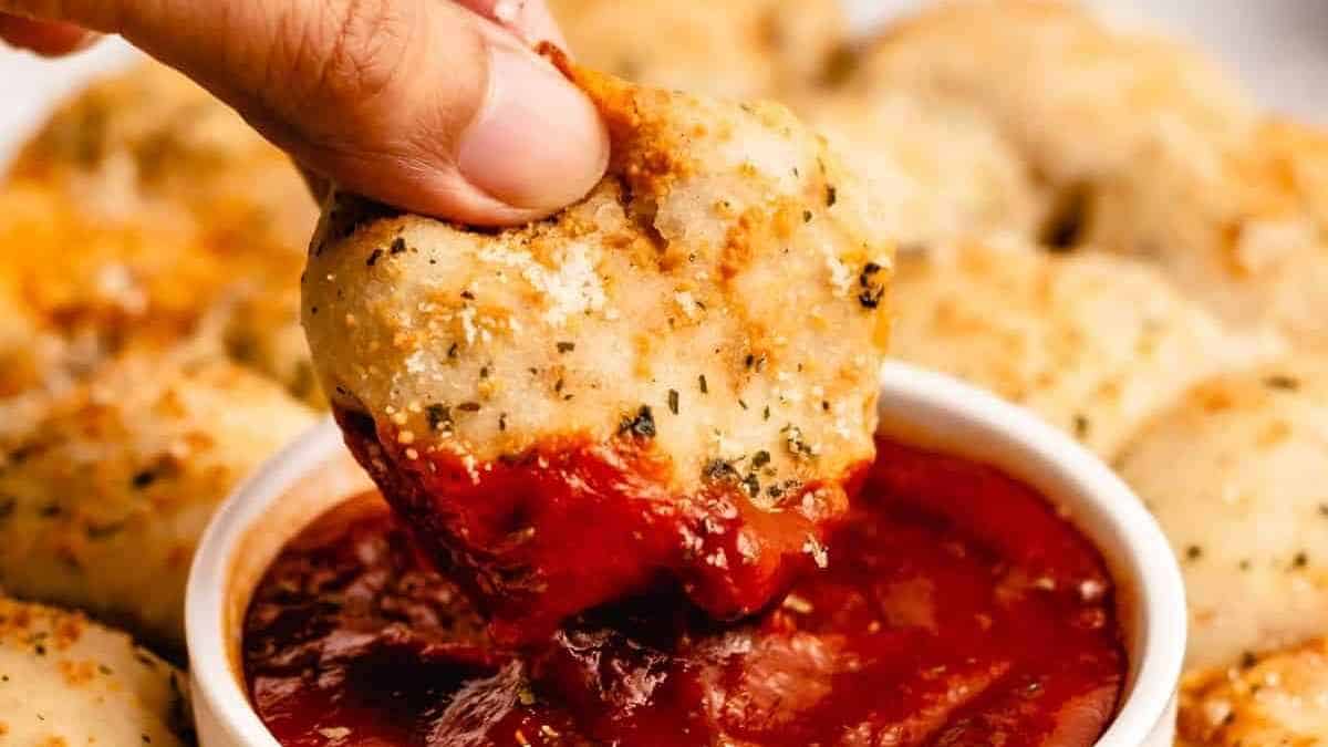 A hand holding a piece of food over a bowl of sauce.
