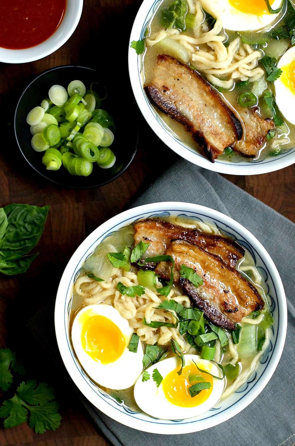 Two bowls of Asian noodle soup with pork belly and an egg on top.