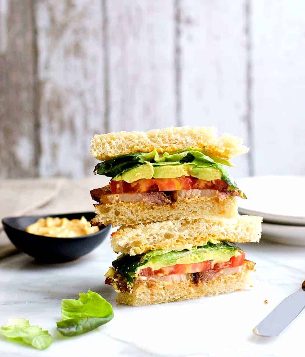 A delectable sandwich with crispy bacon, creamy avocado, and juicy tomato slices, meticulously arranged on a pristine plate.