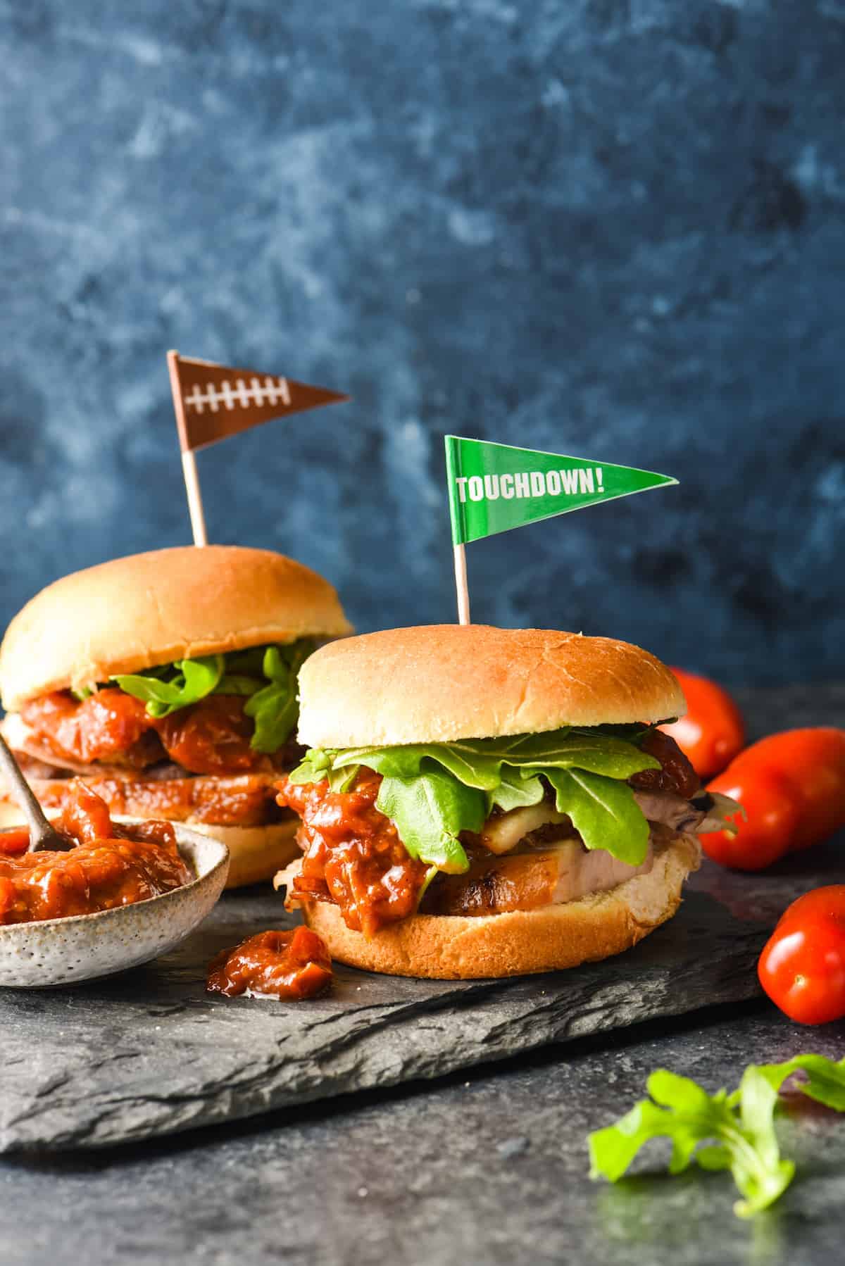 Two football burgers with tomatoes and flags on a slate, perfect for game day.