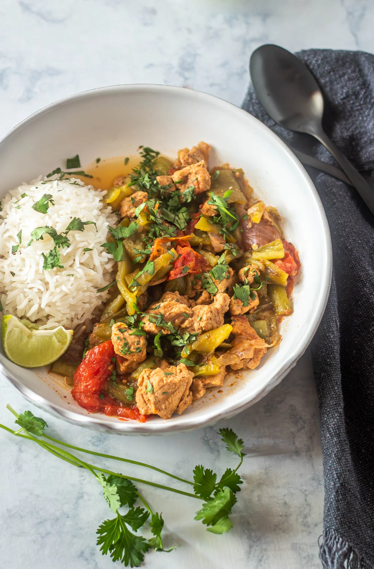 Pork and Hatch Green Chile Stew in a white bowl with rice and lime wedge can be made in a slow cooker or an Instant Pot. 
