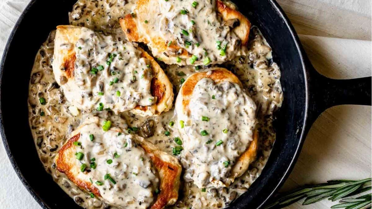 Chicken breasts in a skillet with mushroom gravy and sprigs of rosemary.