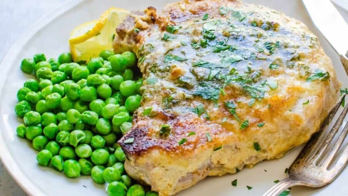 Pork chops on a white plate with peas.