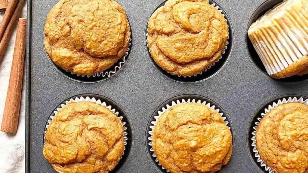Pumpkin muffins in a muffin tin with cinnamon sticks.