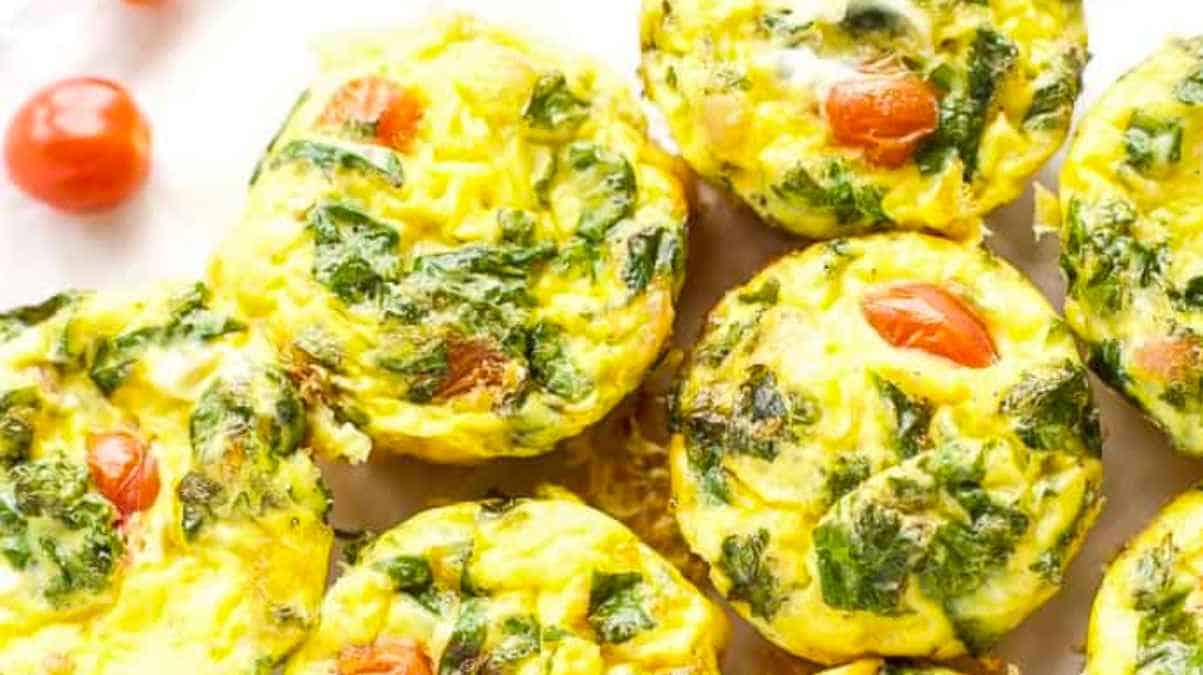 Egg muffins with spinach and tomatoes on a white plate.
