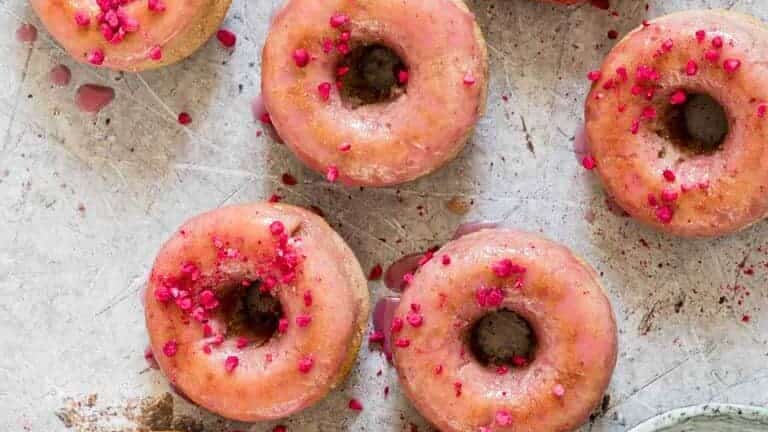 Donuts with pink sprinkles and syrup on a table.
