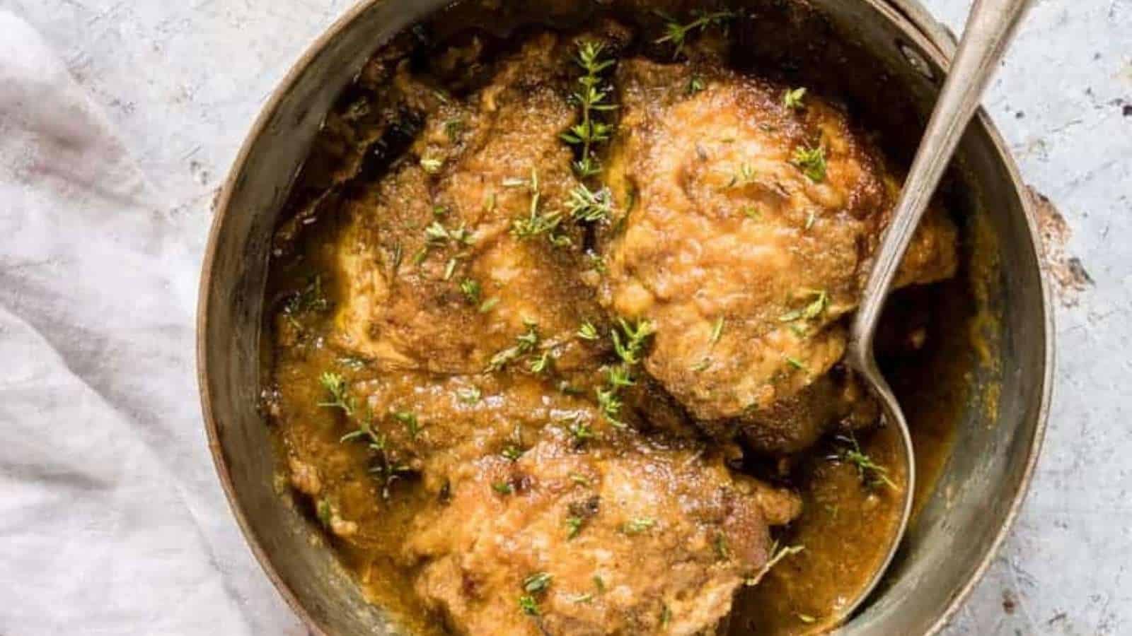 A bowl of chicken in a sauce with thyme sprigs.