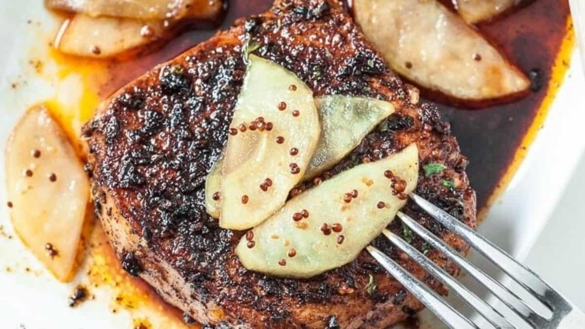 A plate with pork chops and apples on it.