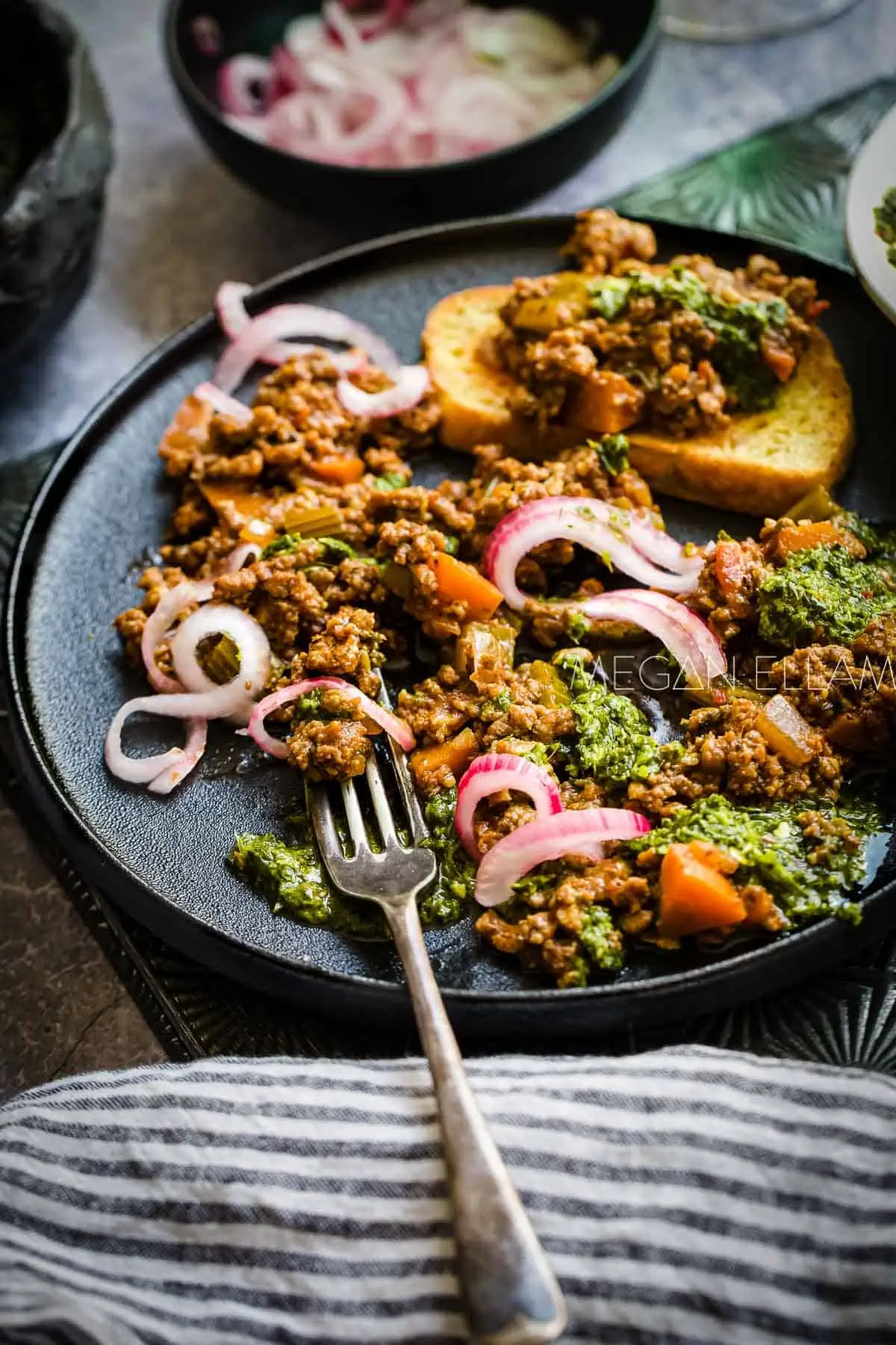 A black plate with minced beef and vegetables on it. 
