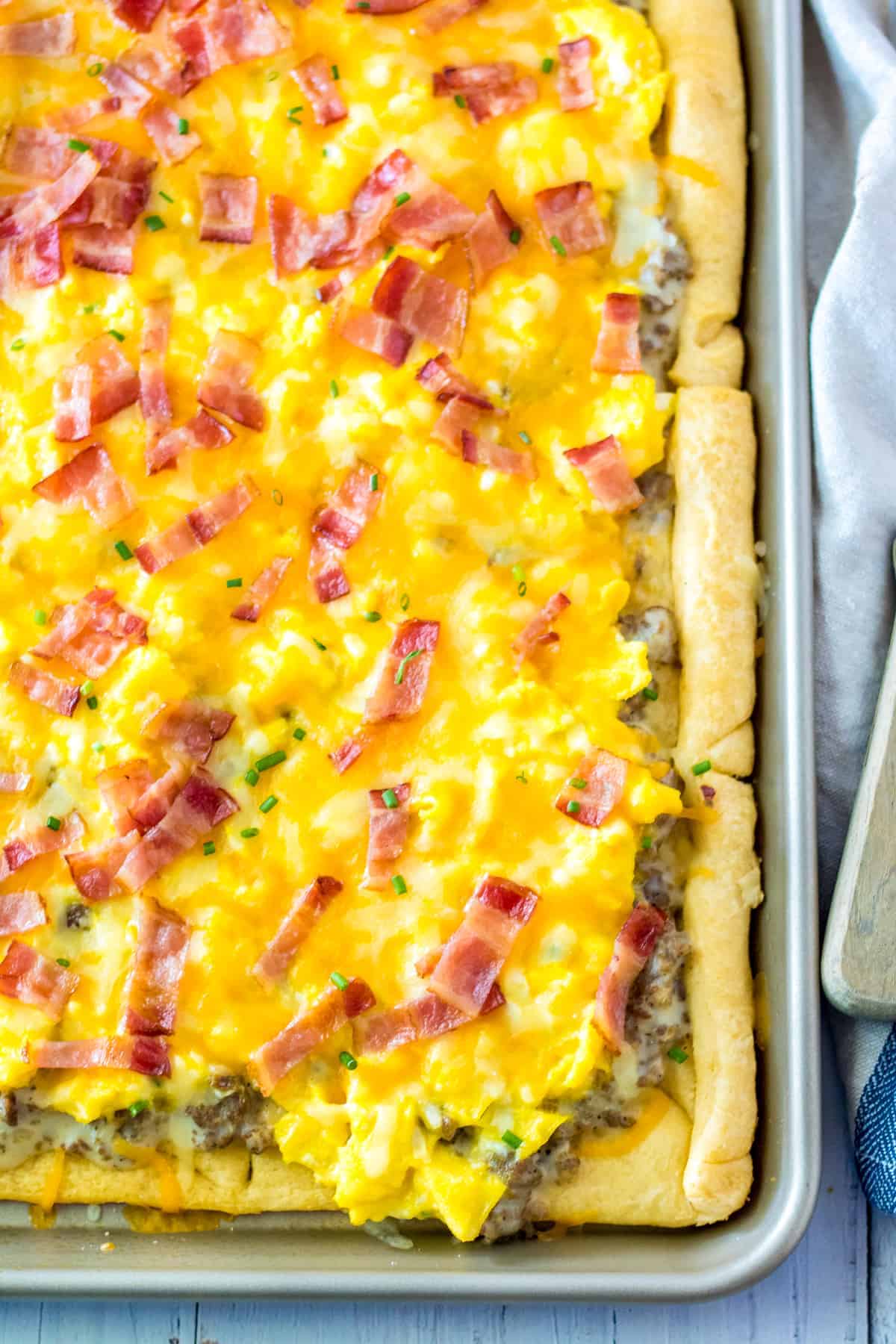 Sheet pan breakfast pizza with crescent roll crust, sausage gravy sauce, scrambled eggs, cheese, and chopped bacon.
