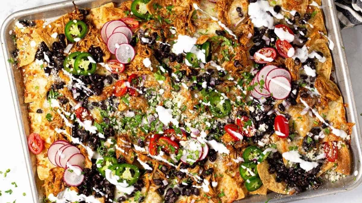 A tray of nachos with black beans, onions and sour cream.