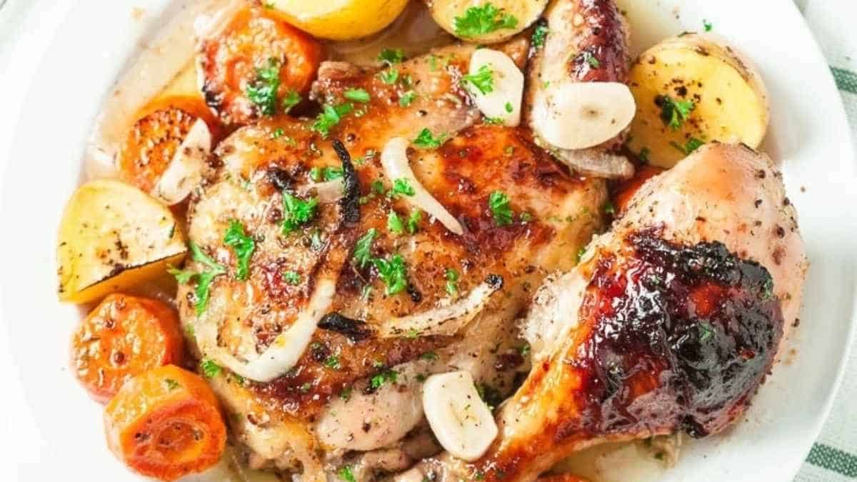 Roasted chicken with potatoes and tomatoes on a white plate.