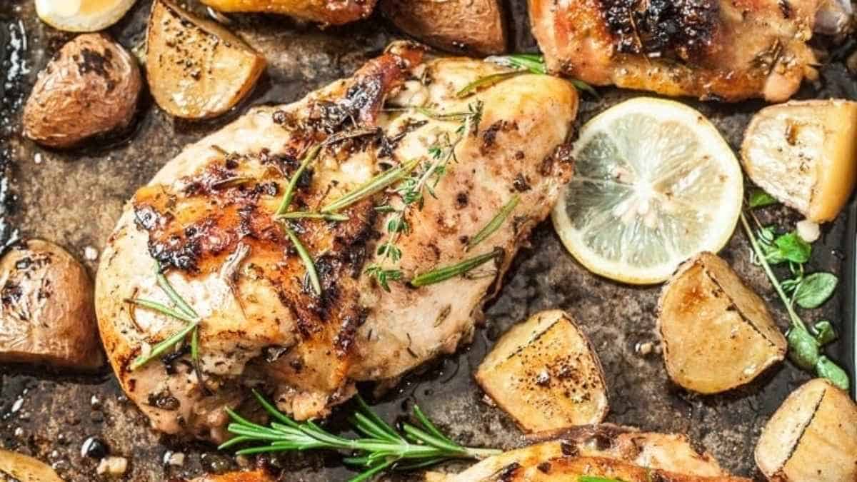 Grilled chicken with lemon and potatoes on a baking sheet.