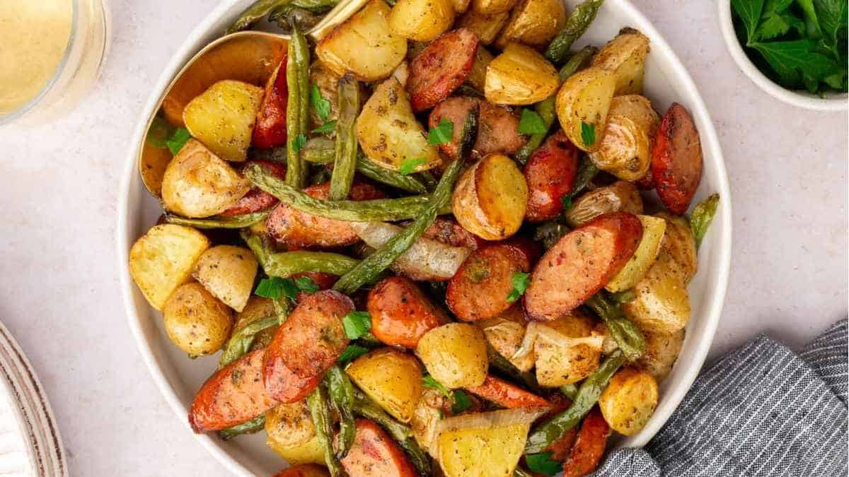 Roasted potatoes and sausages in a white bowl.