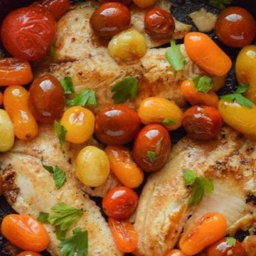 Chicken with tomatoes and herbs in a cast iron skillet.