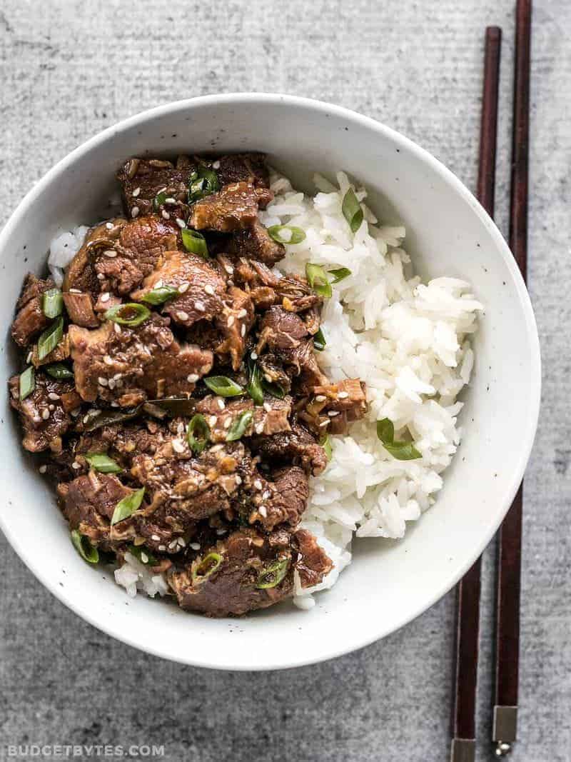 A bowl of beef and rice with chopsticks featuring shaved beef.