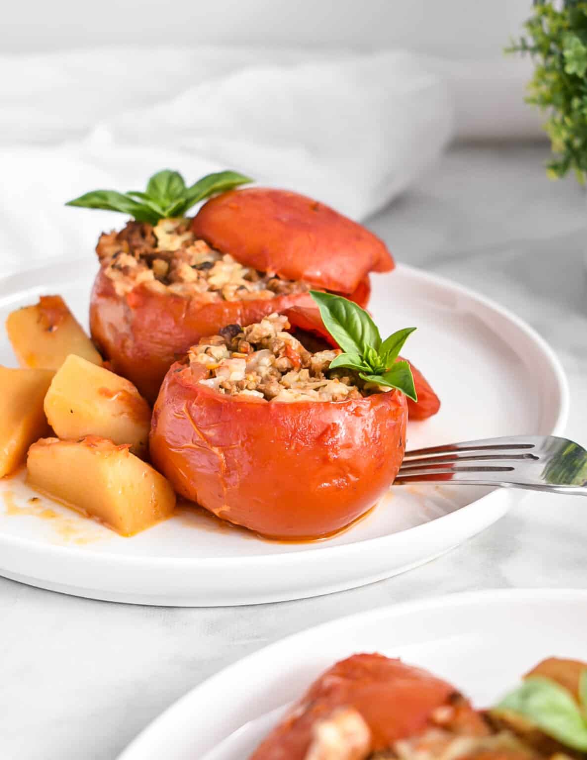 Slow Cooker Stuffed Tomatoes on a plate served with potatoes and topped with basil. 
