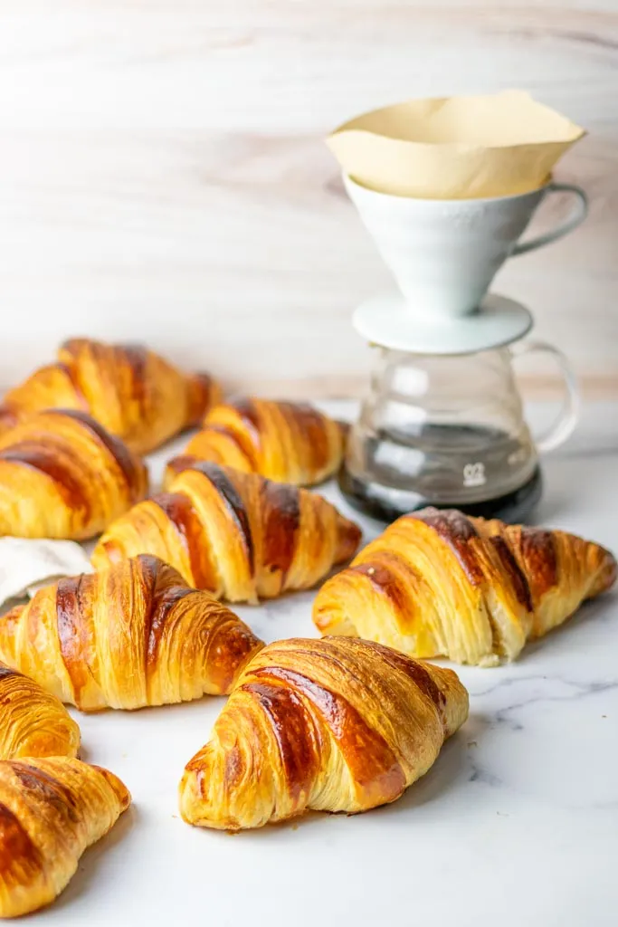 Multiple sourdough croissants on a marble surface with a pour over coffee in background 

