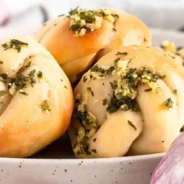 Garlic knots on a plate with garlic and herbs.