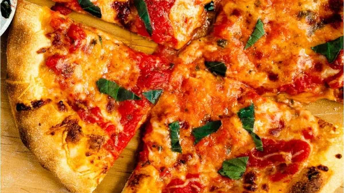 A pizza with tomato sauce and basil on a wooden cutting board.