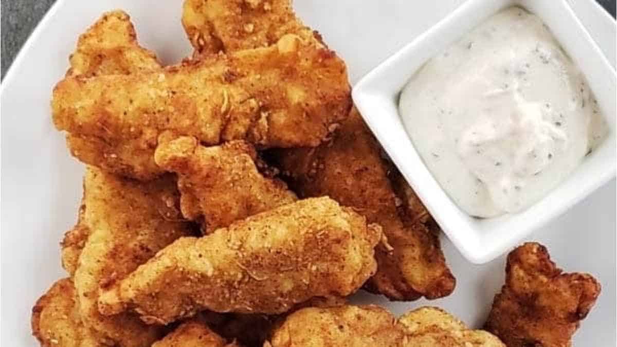Fried chicken nuggets with dipping sauce on a white plate.