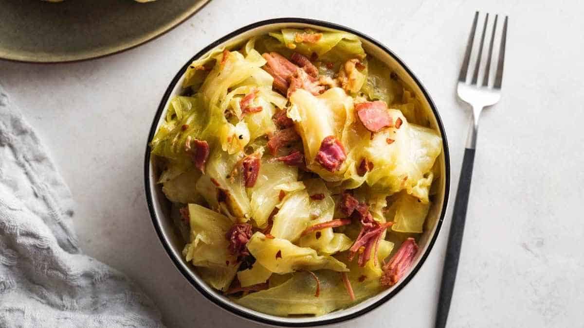 Cabbage and ham in a bowl with a fork.