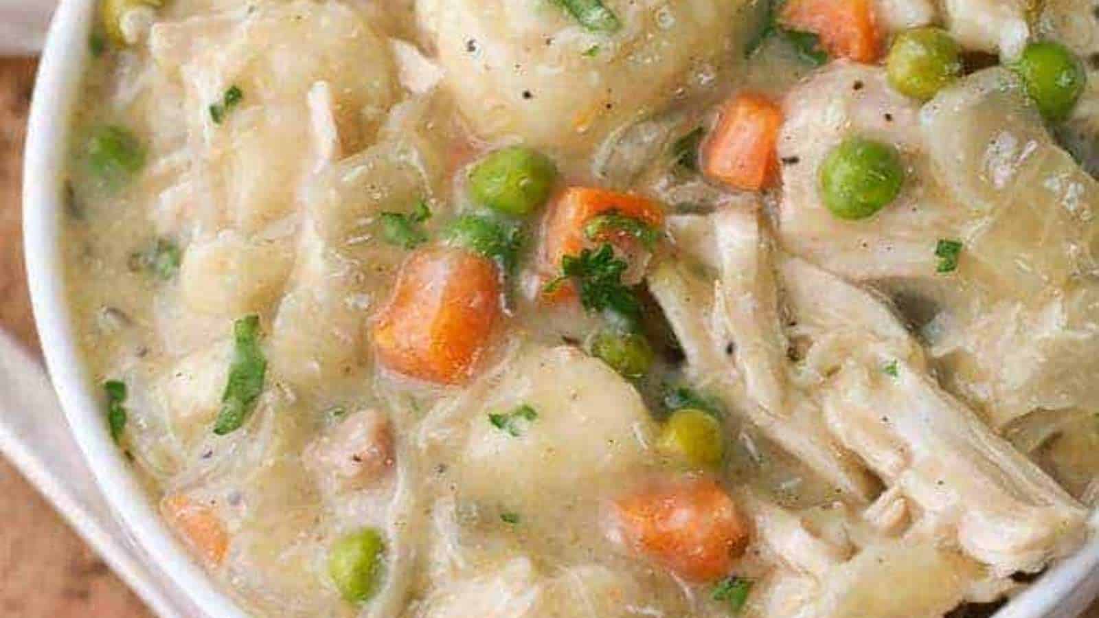 Chicken chowder in a white bowl with carrots and peas.