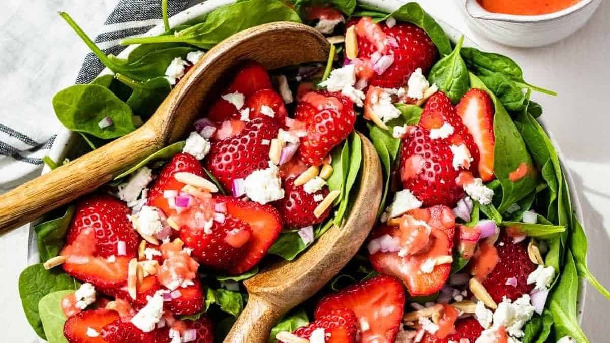 Strawberry spinach salad in a bowl with wooden spoons.
