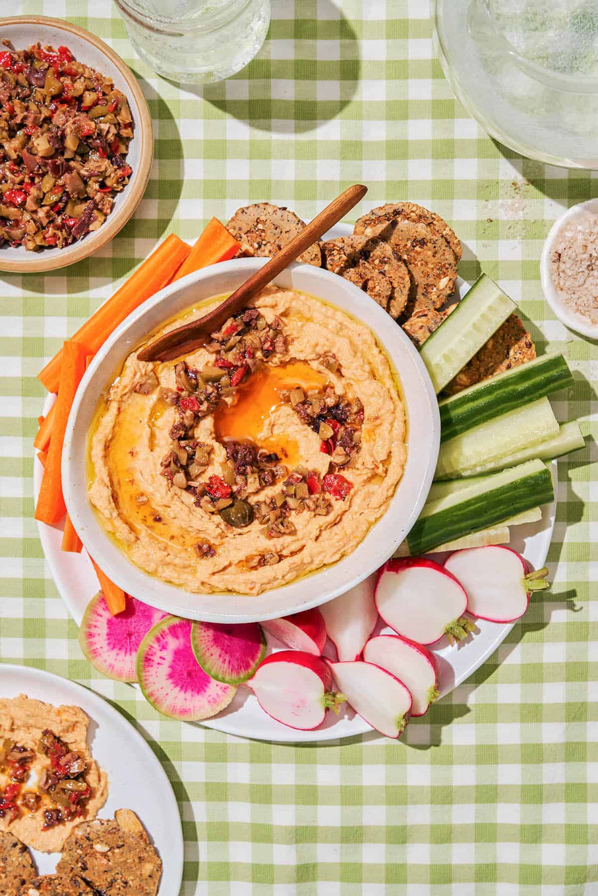 A light orange hummus topped with olive tapenade in a picnic setting. 
