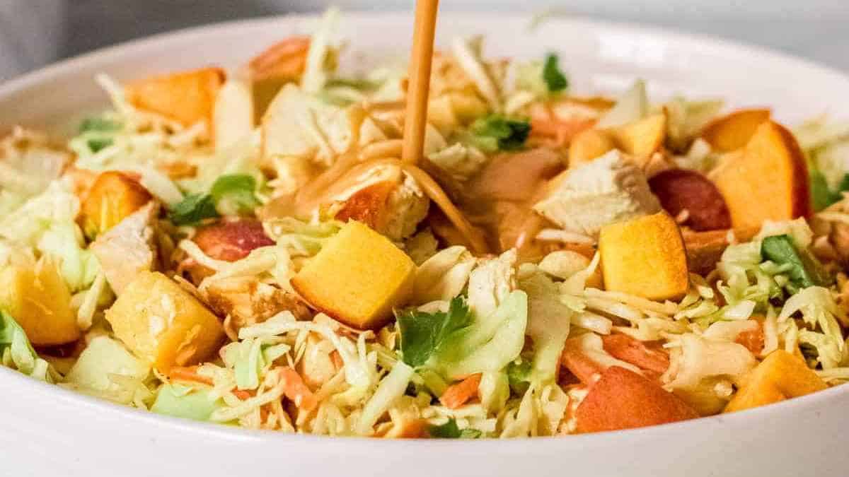 A white bowl with a salad being drizzled with dressing.