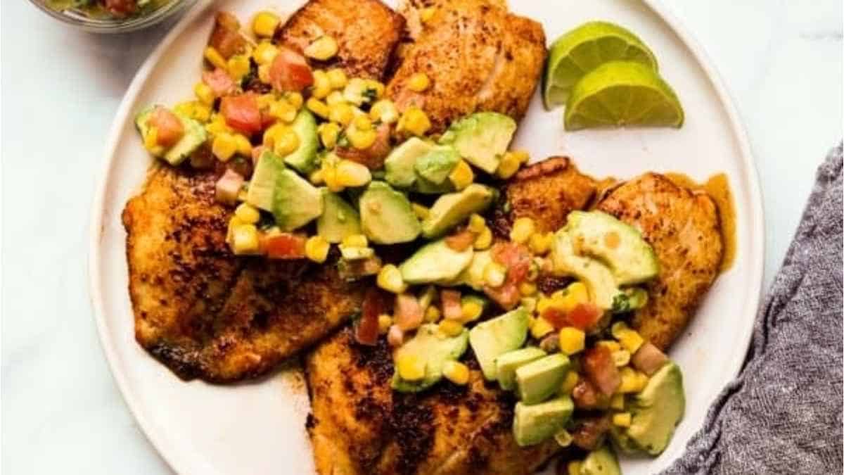 Two fish fillets with avocado and lime on a plate.