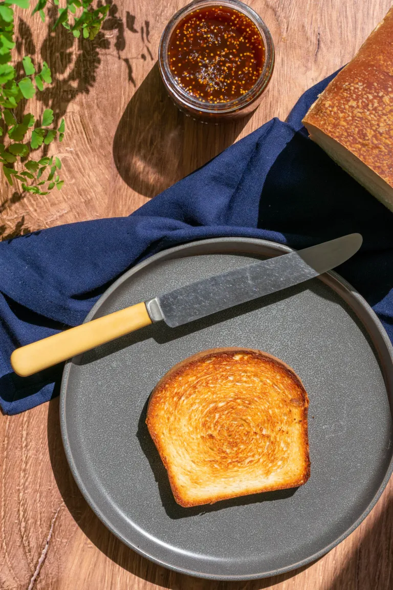 Slice of toasted sourdough sandwich bread on plate with knife and fig jam.

