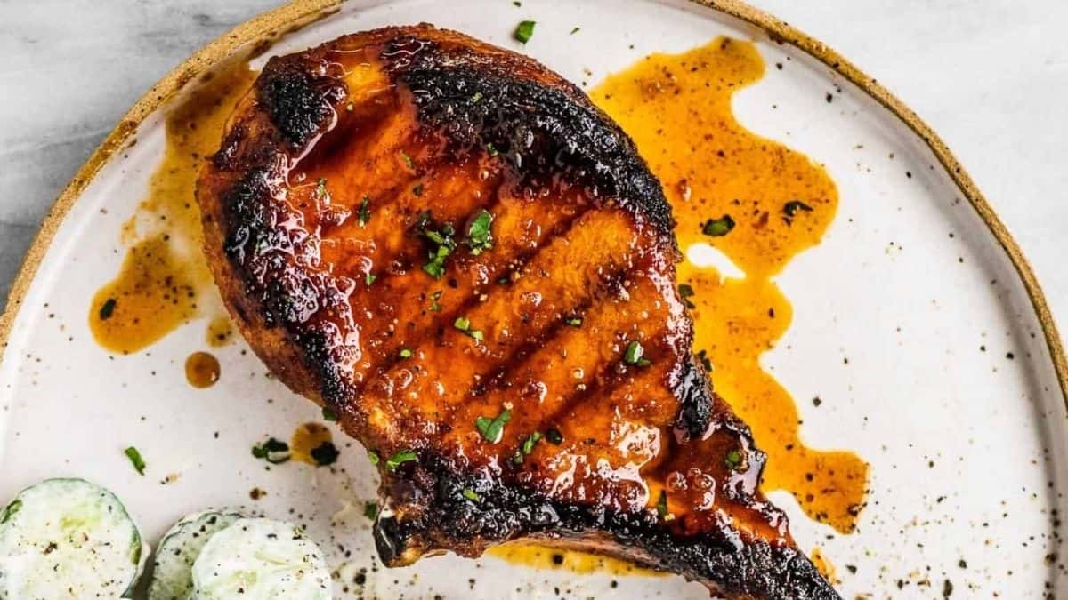Bbq pork chops on a plate with cucumbers and sauce.