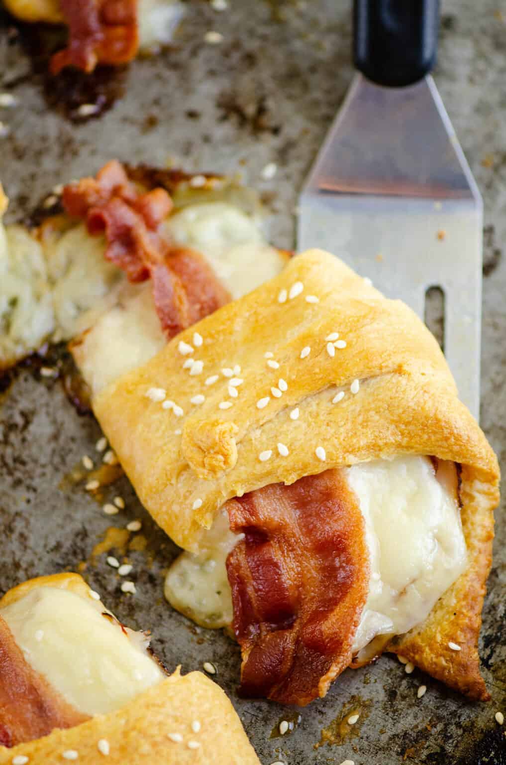 turkey bacon swiss crescent roll on pan with spatula.
