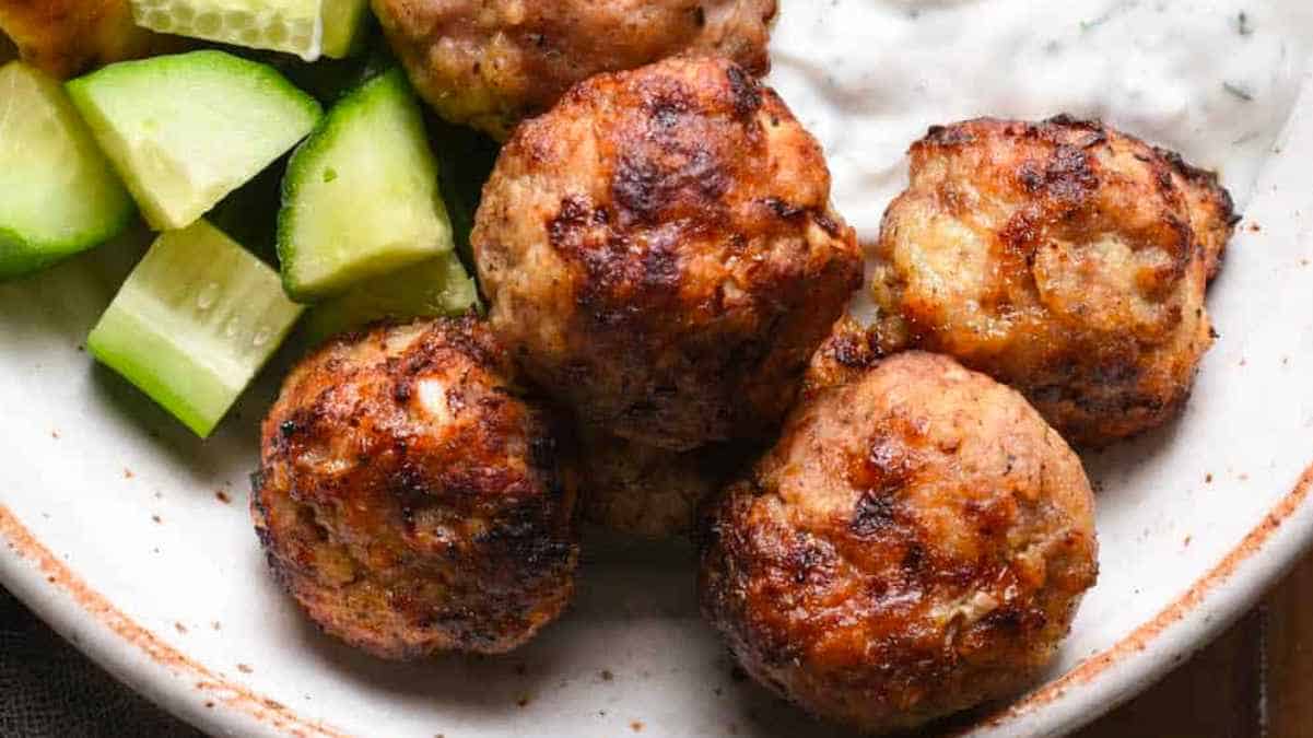 Turkish meatballs on a plate with cucumbers and sour cream.