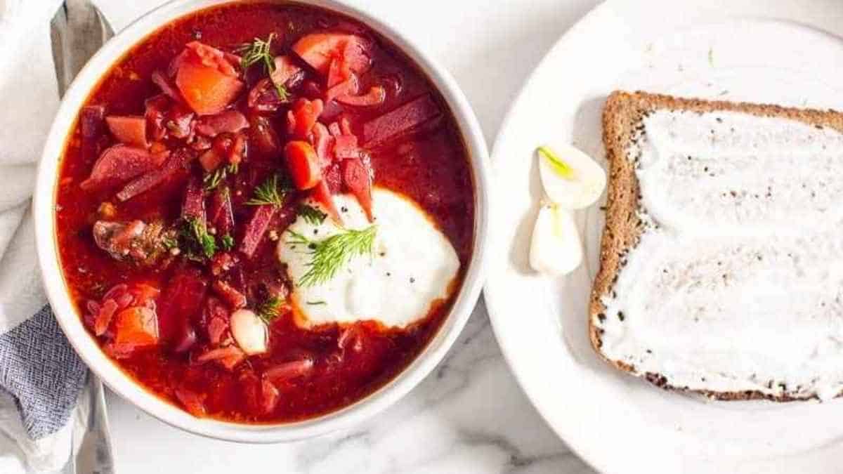 A bowl of beet soup with bread and sour cream.