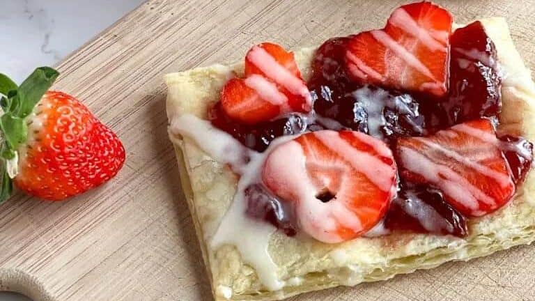 A pastry with strawberries and cream on a cutting board.