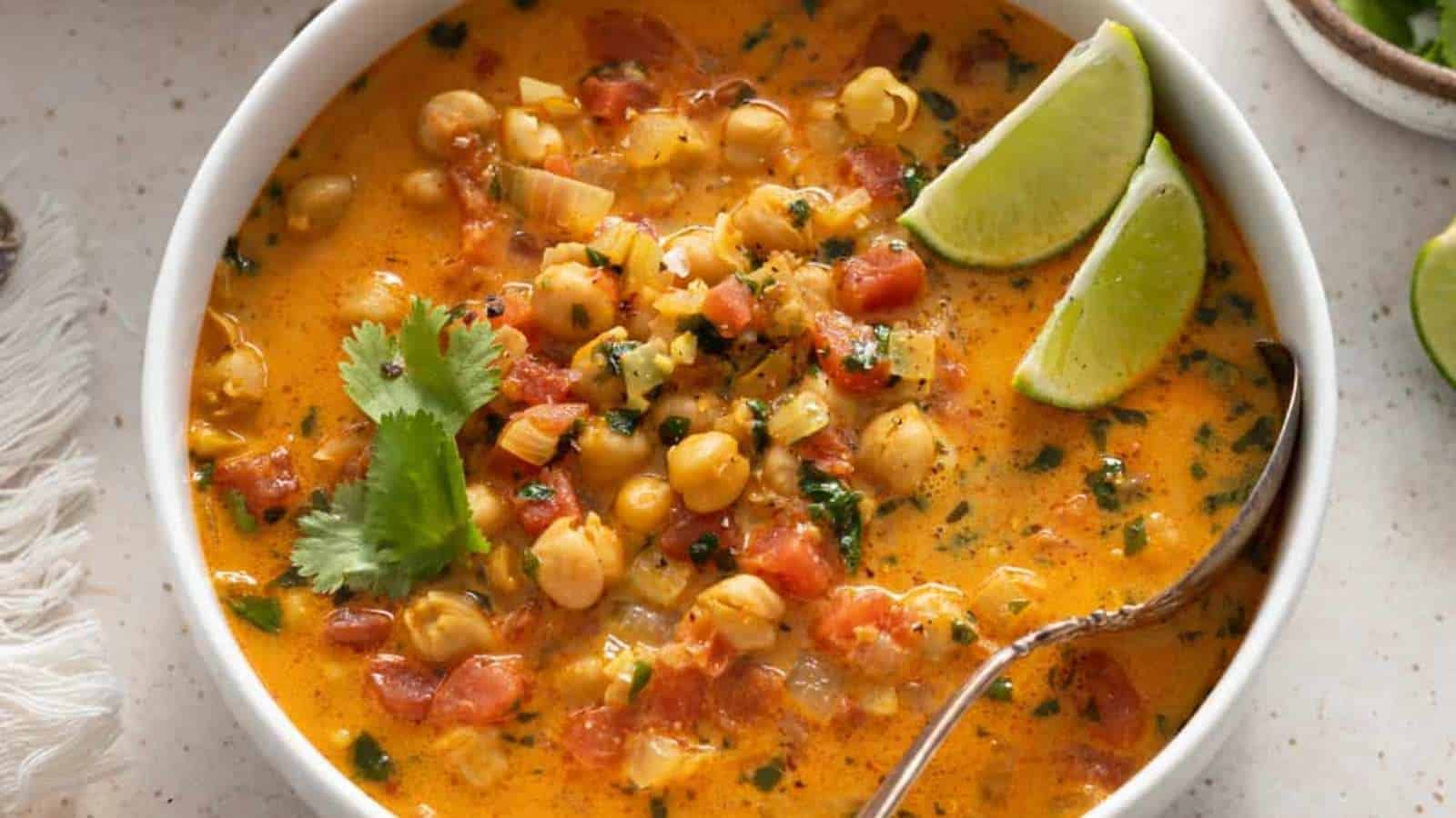 A bowl of chickpea soup with lime wedges.