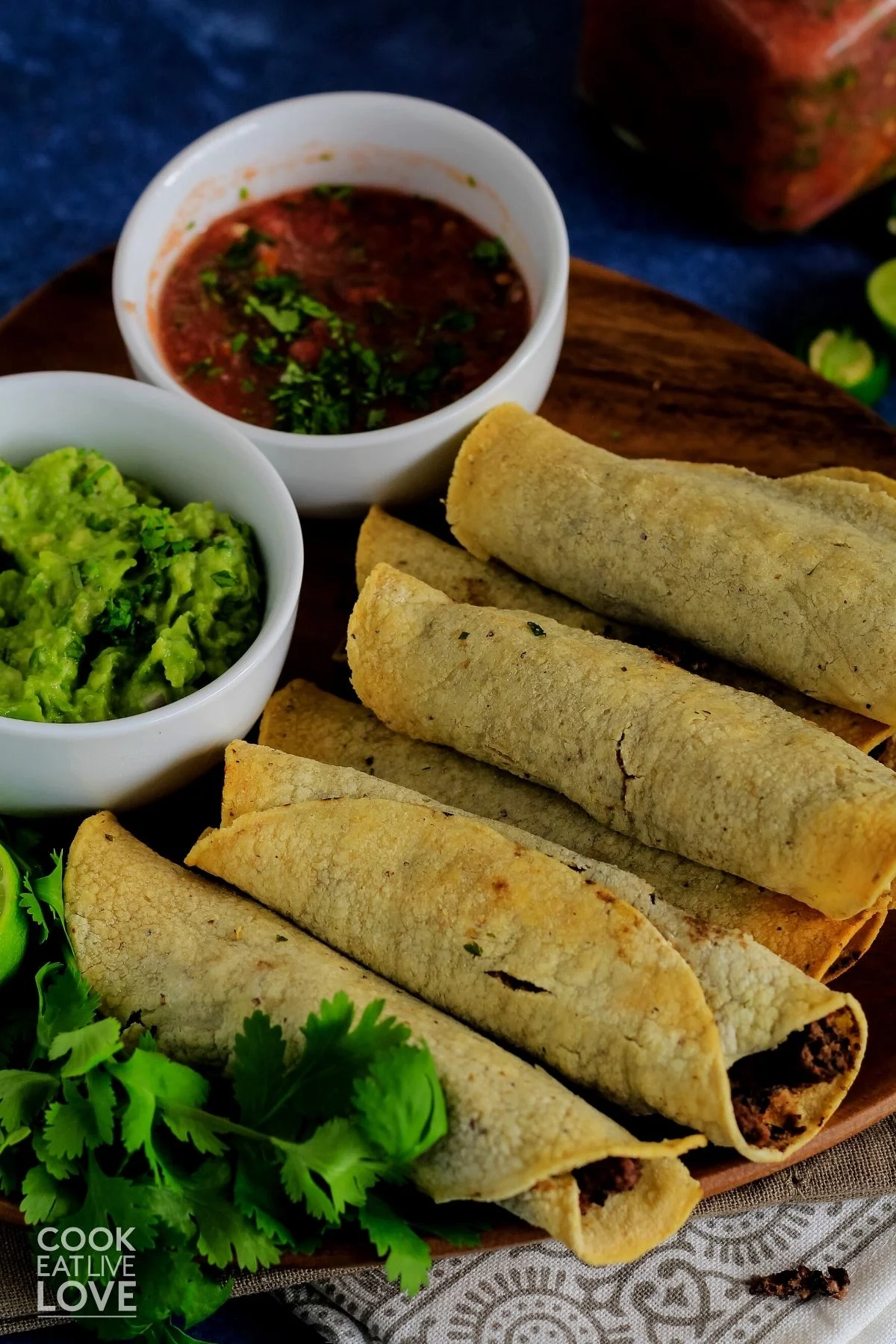 Vegan taquitos on a platter on the table with bowls of salsa and guacamole. 
