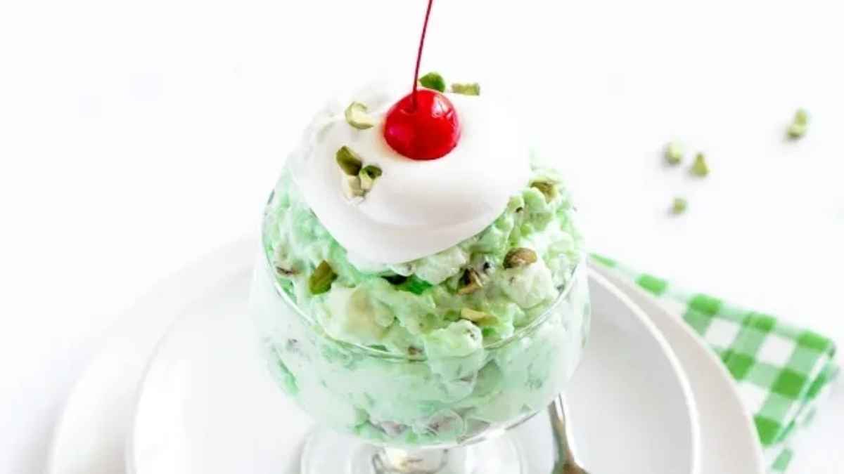 A green dessert with whipped cream and a cherry on top.