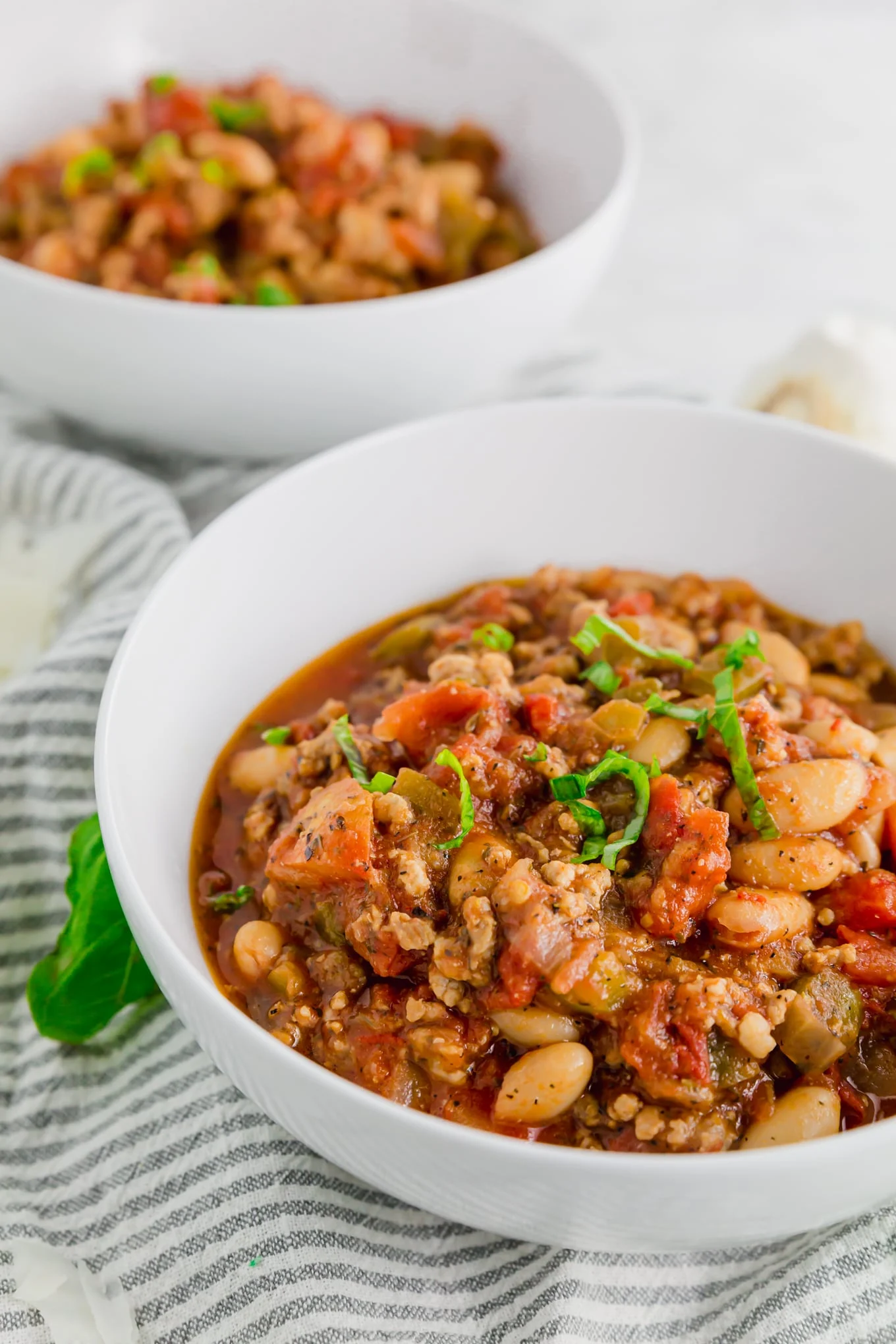 A photo of two bowls of italian sausage stew with white beans topped with fresh basil. / This Italian sausage white bean stew is so easy to make and tastes just like an Italian style chili. It's flavorful and makes for great leftovers! Naturally gluten-free, this stew is great for meal prep or serving guests for a dinner party. Italian sausage white bean stew is hearty, meaty and delicious - perfect for cold winter days. Serve with parmesan cheese and some crusty gluten-free bread. It's ready in 30 minutes when you need a quick weeknight meal! #recipe #glutenfree

