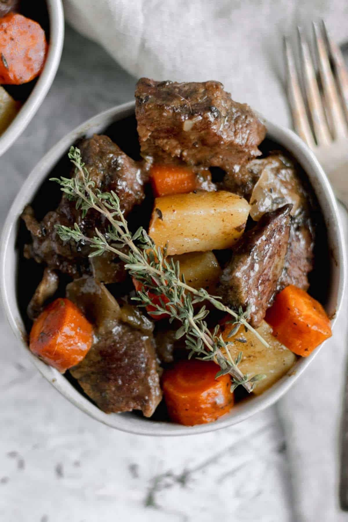 A bowl filled with Whole30 Pot Roast and fresh thyme sprigs sitting on top. 
