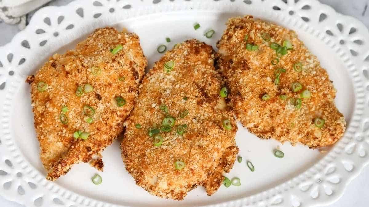 Three fried chicken breasts on a white plate with green onions.