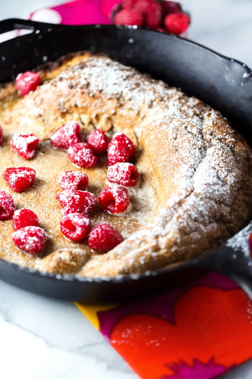 A high protein breakfast skillet filled with raspberry pancakes and powdered sugar.