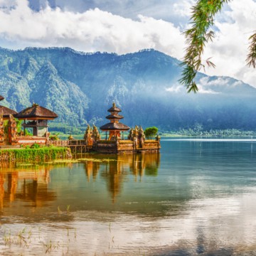 A serene temple in Bali, nestled on the shore of a picturesque lake with majestic mountains as its breathtaking backdrop.